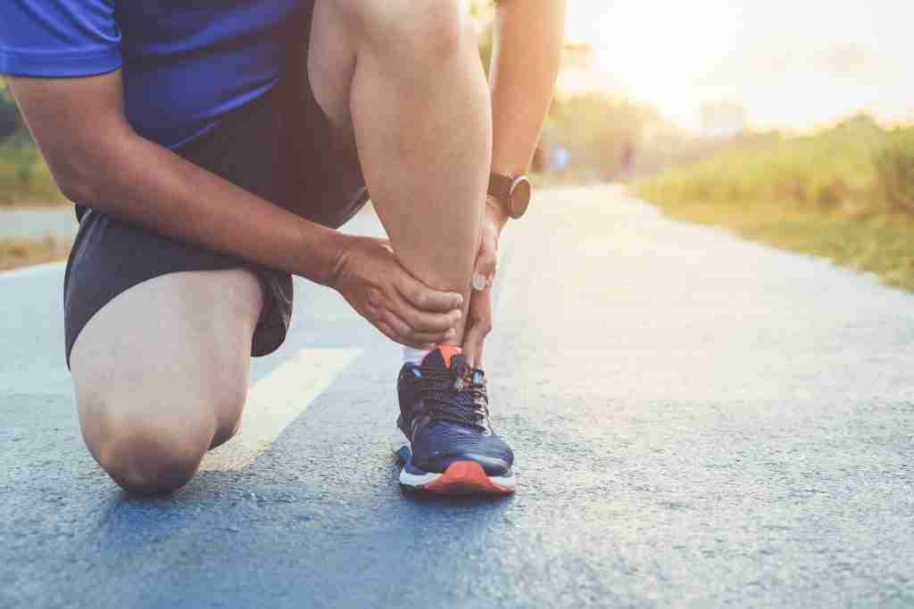 Man holding ankle injured while running. A sprained ankle is one of the answers to the question of when to use kinesiology tape.