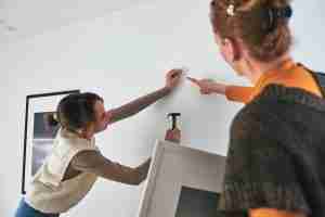 A mother and daughter using a hammer to hang photos on a wall.