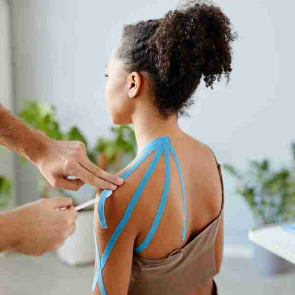 Close up image of therapist putting k tape on shoulder of young African American woman in physiotherapy clinic