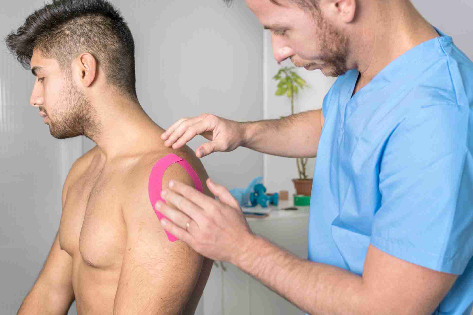 Physical therapist applying kinesiology tape to male patient's shoulder
