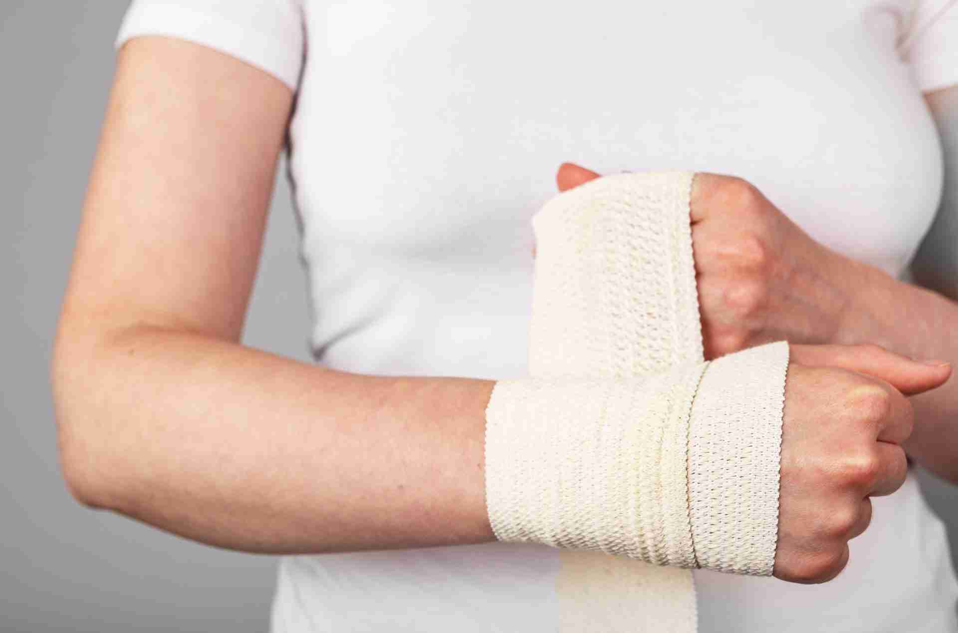Close up image of woman applying elastic tape bandage to her injured wrist.